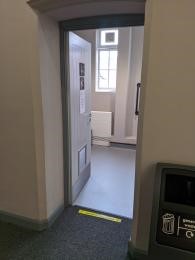 An open door leading into a public toilet with grey lino
