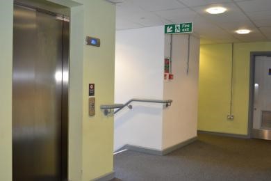 Silver lift doors surrounded by lime green walls, next to a stairwell